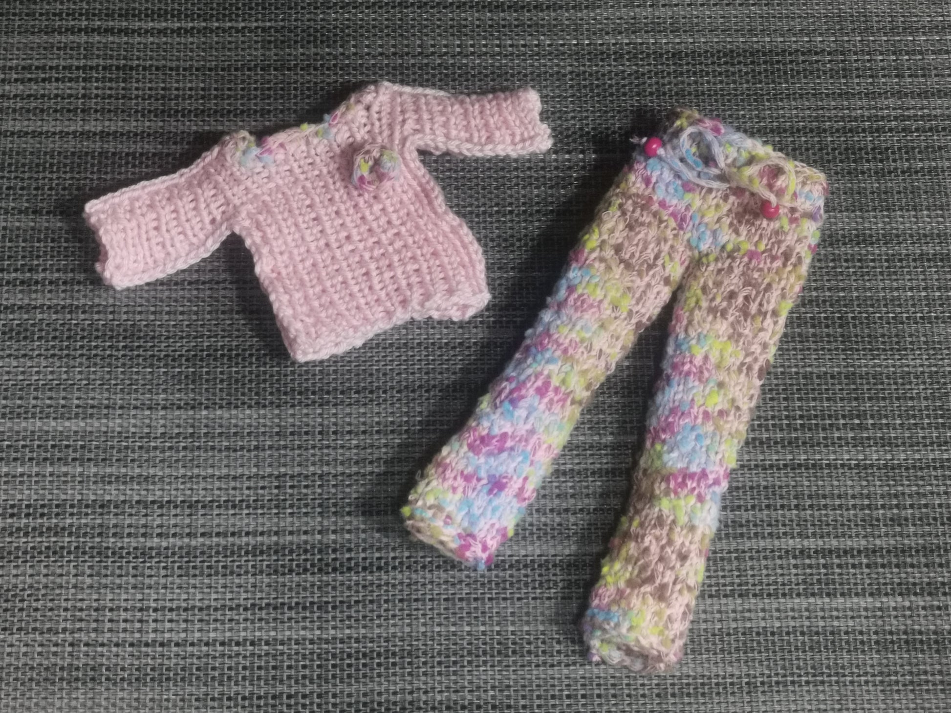 Gestricktes Barbie-Outfit in bunten Farben, bestehend aus Pulli und Hose – handgefertigte Kleidung für Puppen.